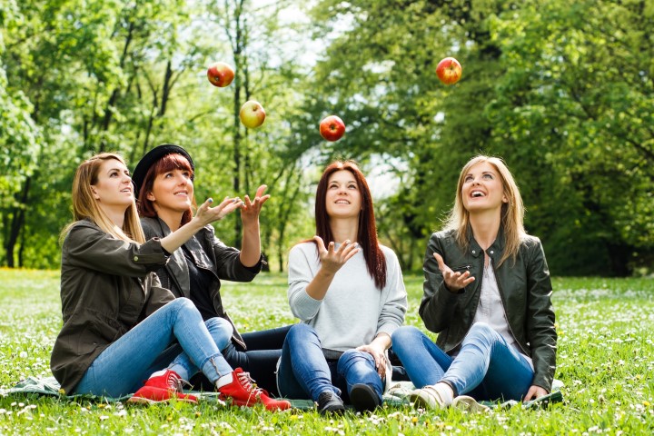 Vier vrouwen zittend in het gras gooien lachend een appel in de lucht